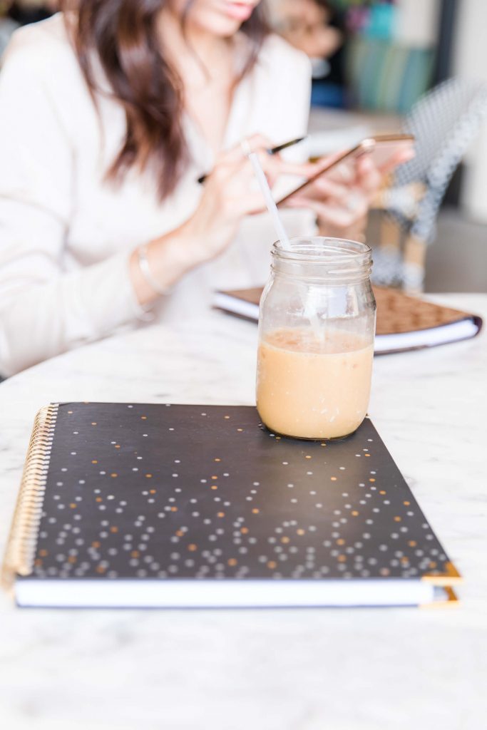 black notebook with mason jar of iced coffee girl in background